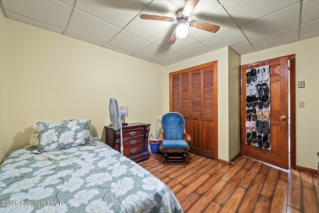 bedroom with a paneled ceiling, a closet, a ceiling fan, wood finished floors, and baseboards