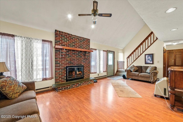 living room with lofted ceiling, a fireplace, wood finished floors, stairs, and baseboard heating