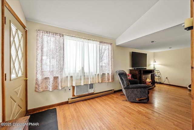 living area featuring baseboards, a glass covered fireplace, a baseboard radiator, wood-type flooring, and vaulted ceiling