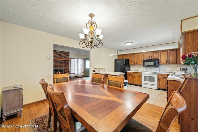 dining space with a fireplace, a notable chandelier, light wood-style flooring, and a textured ceiling