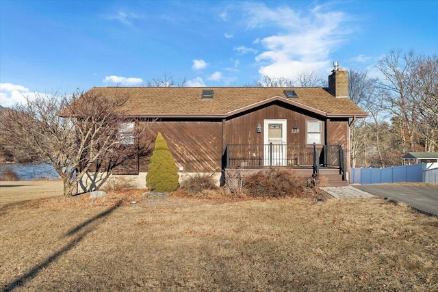 view of front of house with a shingled roof, a chimney, fence, and a front yard