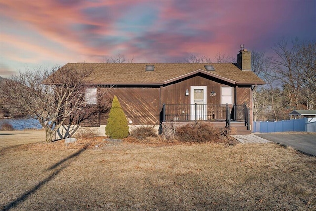 view of front of house featuring a front lawn, a chimney, a shingled roof, and fence