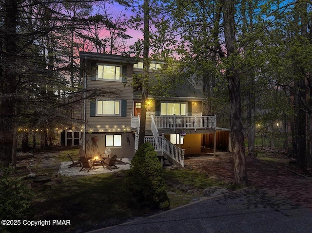 back of property at dusk featuring a fire pit, a deck, a patio area, and stairs