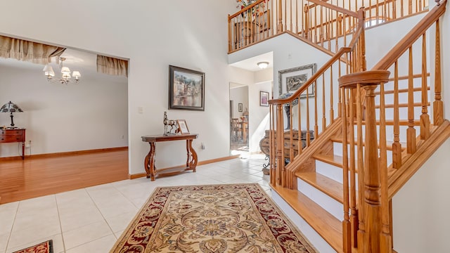 entrance foyer with baseboards, stairway, an inviting chandelier, tile patterned flooring, and a high ceiling