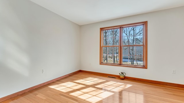 spare room with wood-type flooring, visible vents, and baseboards