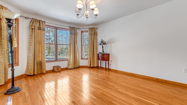 spare room with baseboards, hardwood / wood-style floors, and a notable chandelier