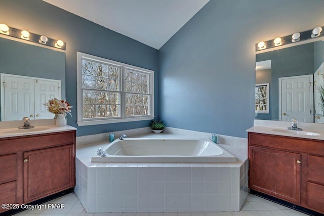 bathroom with a garden tub, vaulted ceiling, two vanities, and a sink