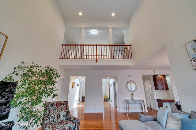 living room featuring decorative columns, baseboards, wood finished floors, a high ceiling, and recessed lighting