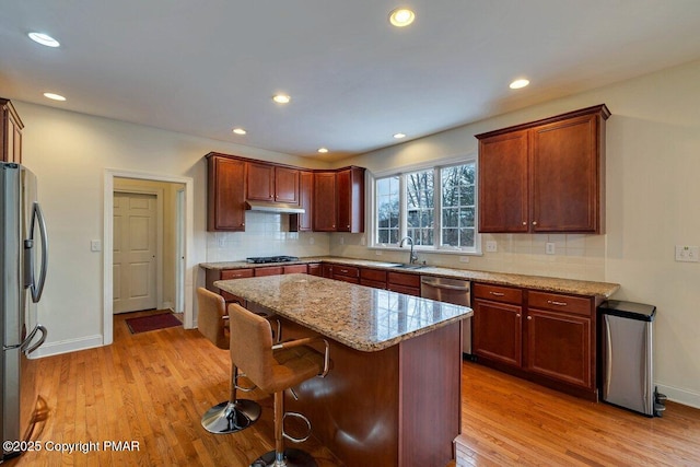 kitchen with light wood finished floors, backsplash, stainless steel appliances, a kitchen bar, and a sink