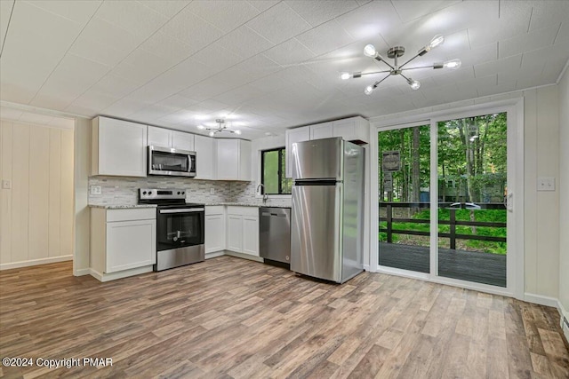 kitchen with stainless steel appliances, decorative backsplash, wood finished floors, and an inviting chandelier