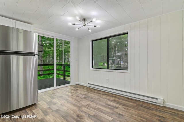 spare room featuring a chandelier, baseboard heating, wood finished floors, and a healthy amount of sunlight