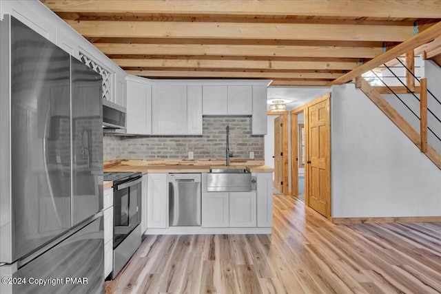 kitchen featuring stainless steel appliances, a sink, white cabinetry, light wood-type flooring, and tasteful backsplash