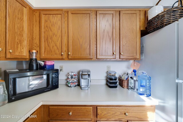 kitchen featuring brown cabinets, freestanding refrigerator, black microwave, and light countertops