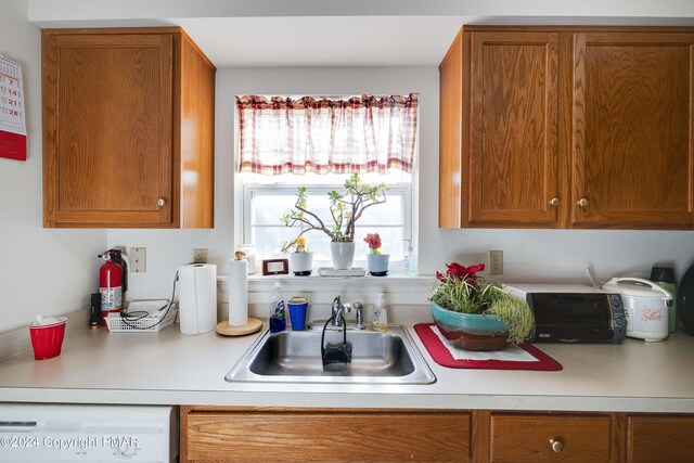 kitchen featuring a sink, brown cabinetry, light countertops, and dishwasher