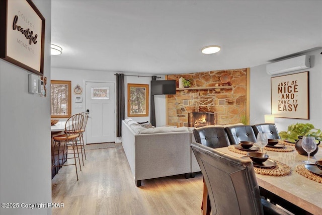 living room with a stone fireplace, a wall unit AC, and light wood-type flooring