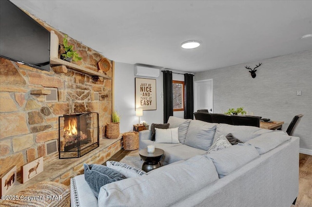 living room with an AC wall unit, a fireplace, and light hardwood / wood-style flooring