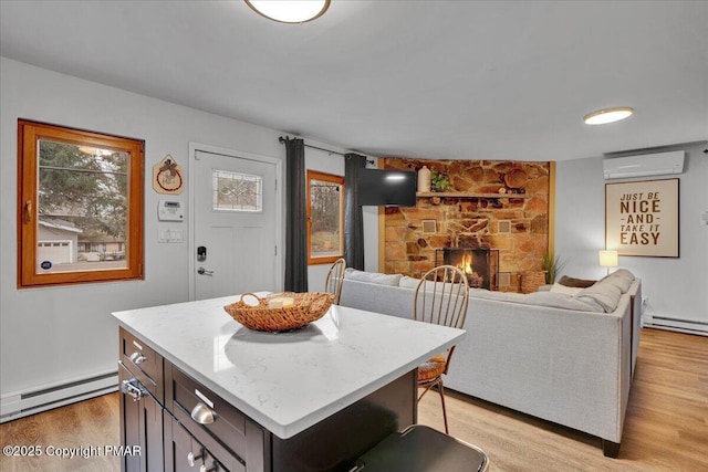 kitchen with a wall unit AC, a center island, a stone fireplace, a baseboard radiator, and light wood-type flooring