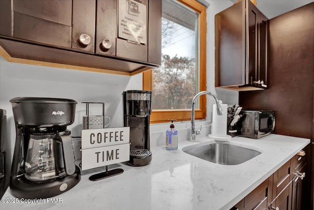 kitchen featuring light stone counters, dark brown cabinets, and a sink