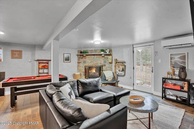 living room featuring pool table, a wall mounted air conditioner, a stone fireplace, and light hardwood / wood-style floors