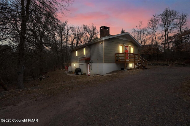 property exterior at dusk featuring cooling unit, dirt driveway, and a chimney