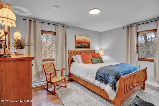 bedroom featuring hardwood / wood-style flooring, a baseboard radiator, and multiple windows