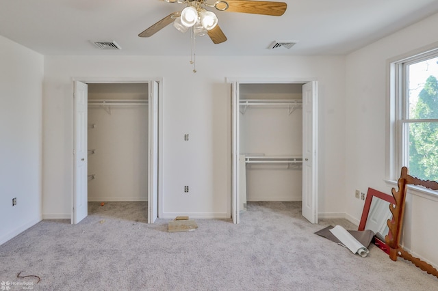 unfurnished bedroom featuring visible vents, carpet, ceiling fan, and two closets