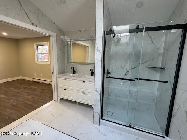 bathroom featuring double vanity, a marble finish shower, marble finish floor, baseboard heating, and a sink