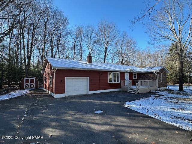 view of front of property with an attached garage, an outdoor structure, driveway, a shed, and a chimney