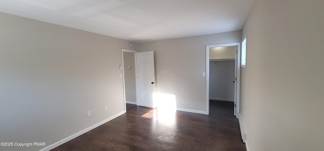 unfurnished bedroom featuring a walk in closet, dark wood-type flooring, baseboards, and a closet