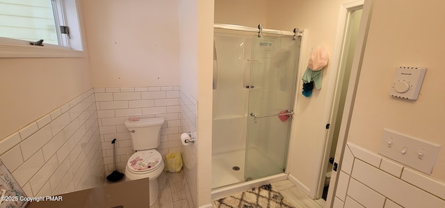 bathroom with a wainscoted wall, a stall shower, toilet, and tile walls