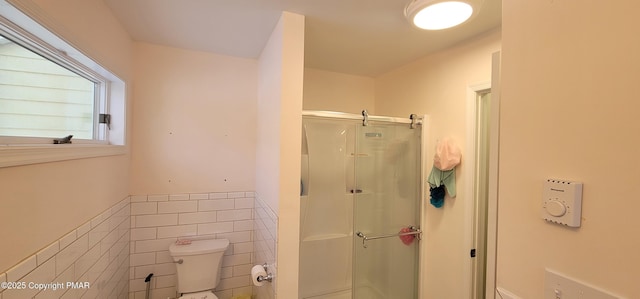 bathroom with toilet, tile walls, a stall shower, and wainscoting