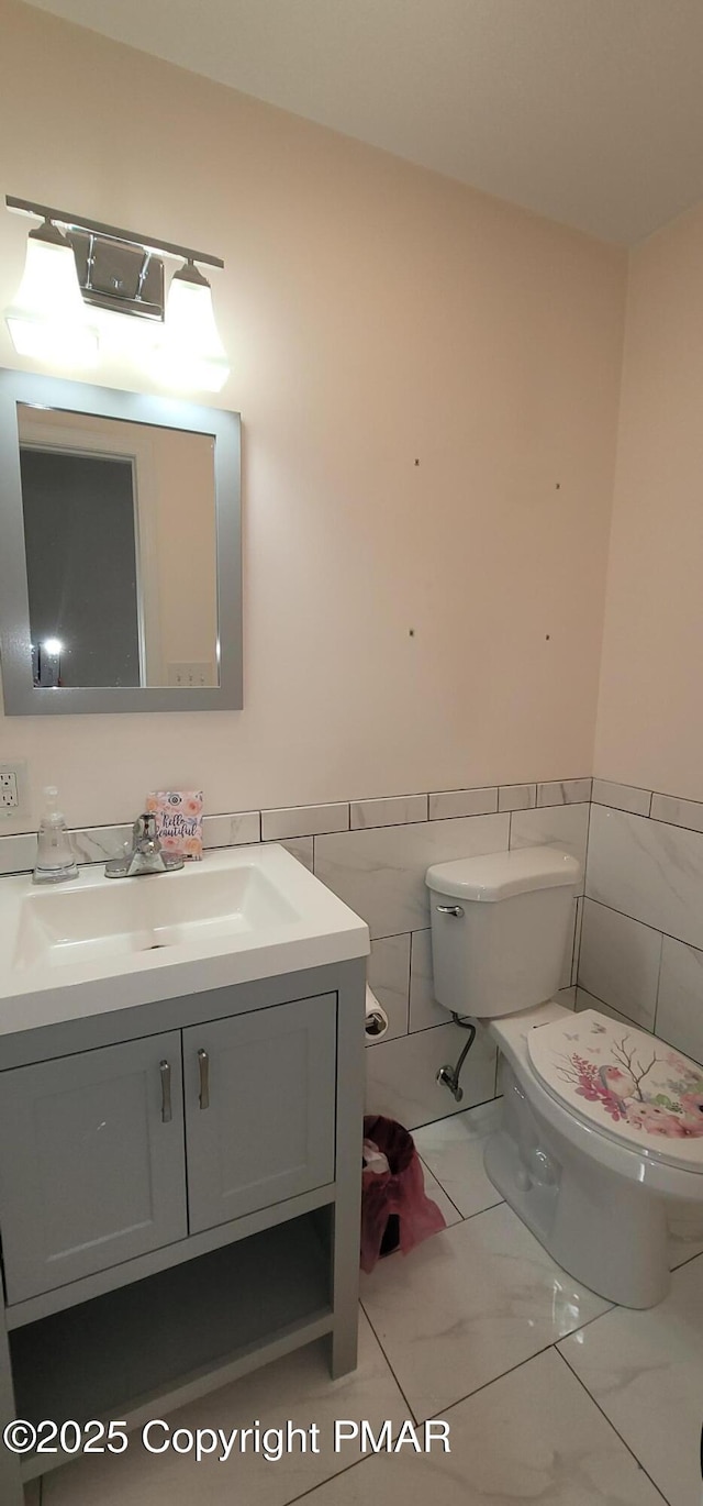 bathroom featuring vanity, a wainscoted wall, tile walls, toilet, and marble finish floor