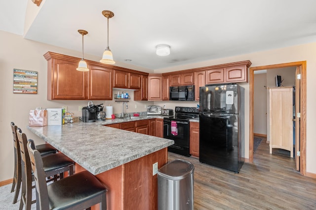 kitchen featuring brown cabinetry, a breakfast bar, a peninsula, a sink, and black appliances