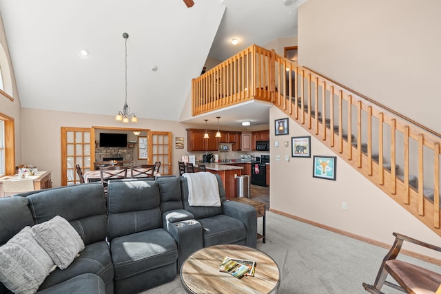 living room featuring high vaulted ceiling, a stone fireplace, baseboards, light colored carpet, and stairs