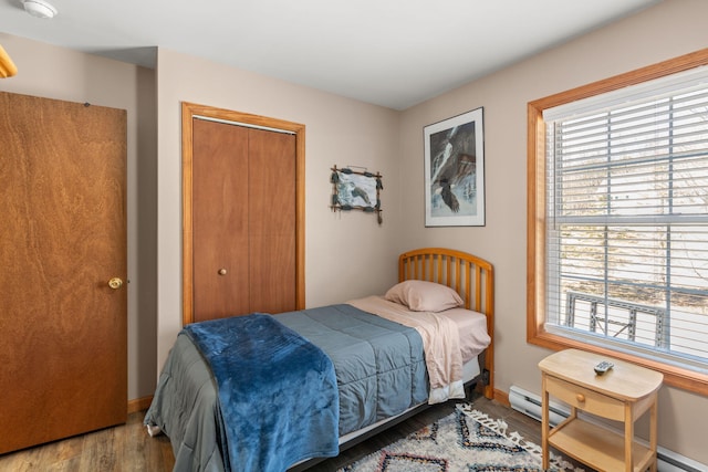 bedroom with a closet, multiple windows, wood finished floors, and a baseboard radiator