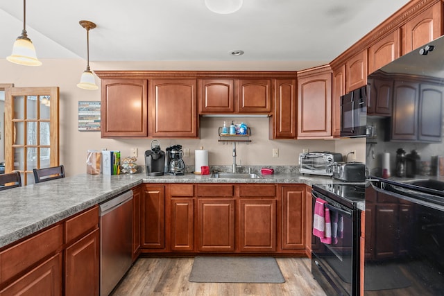 kitchen featuring black appliances, a sink, brown cabinetry, light wood finished floors, and hanging light fixtures