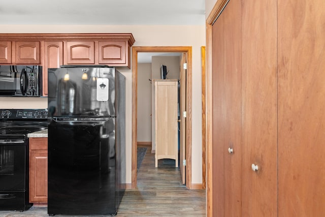 kitchen featuring black appliances, brown cabinetry, wood finished floors, and baseboards