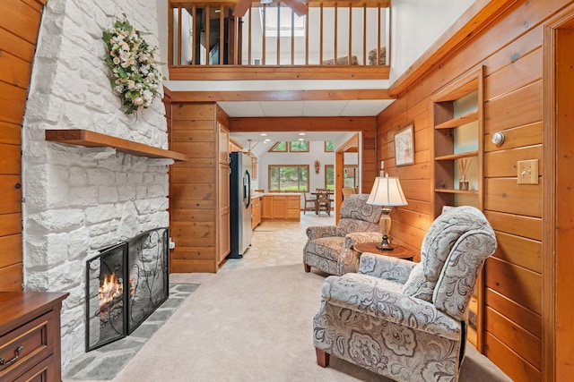 living room with a stone fireplace, light colored carpet, wood walls, and a high ceiling