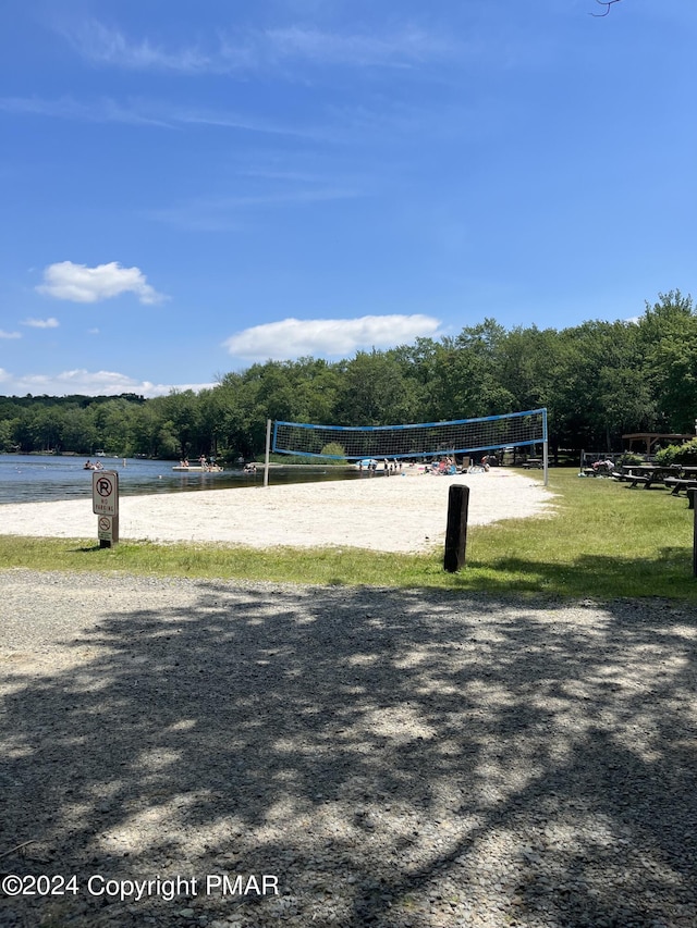 surrounding community with a forest view, a lawn, and volleyball court