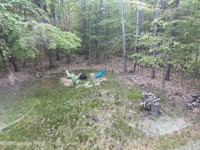 view of yard featuring an outdoor fire pit and a wooded view