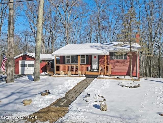 view of front of home with an outbuilding, a porch, a detached garage, driveway, and a chimney