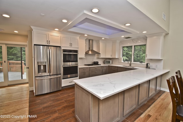 386 Camelback Rd, Tannersville, PA 18372 - kitchen featuring wall chimney exhaust hood, a sink, appliances with stainless steel finishes, a peninsula, and white cabinetry