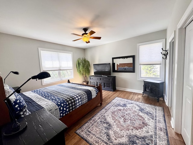 bedroom with baseboards, a wood stove, wood finished floors, and multiple windows