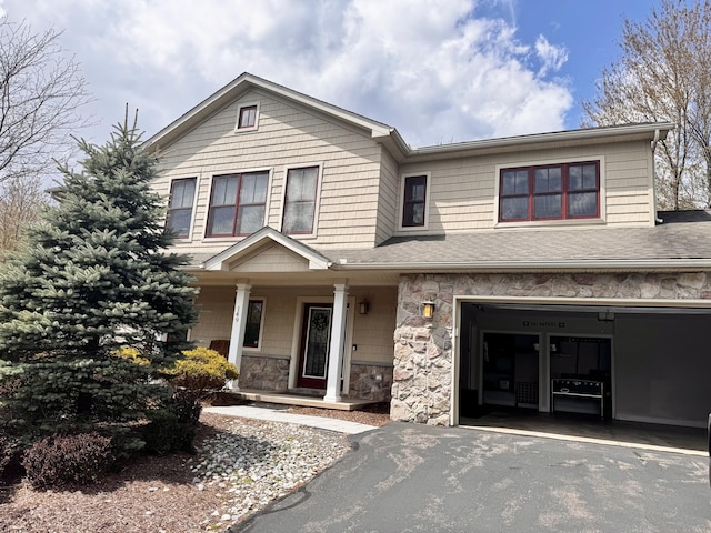 view of front of home featuring covered porch, an attached garage, driveway, and stone siding