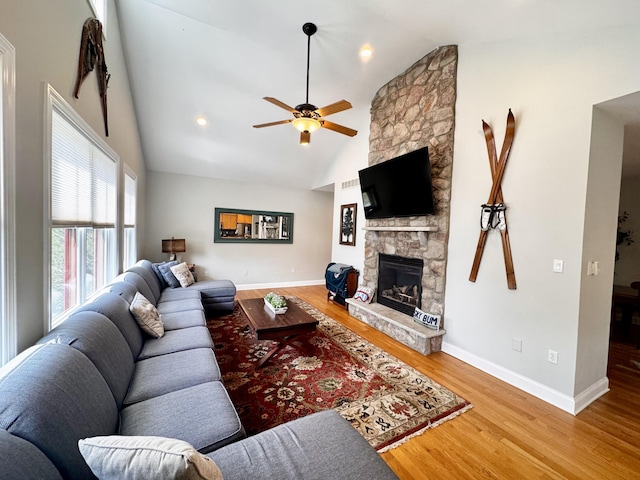 living room with high vaulted ceiling, a stone fireplace, a ceiling fan, baseboards, and wood finished floors