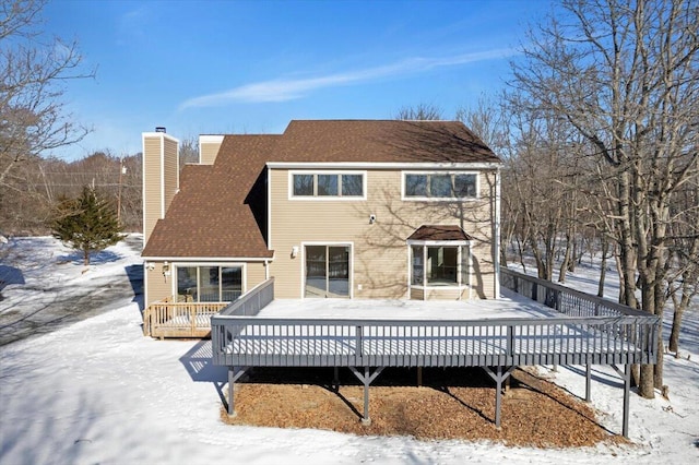 snow covered rear of property with a chimney and a deck