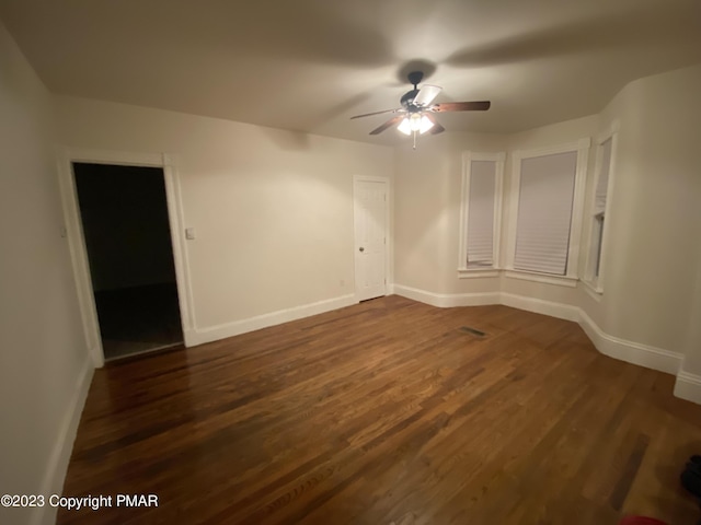 spare room featuring dark wood-type flooring, baseboards, and a ceiling fan