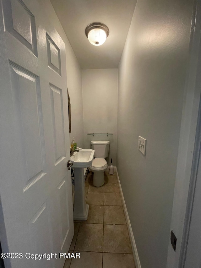 half bath with tile patterned flooring, toilet, and baseboards