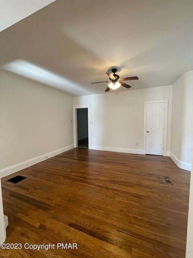 empty room with a ceiling fan, baseboards, visible vents, and dark wood-type flooring