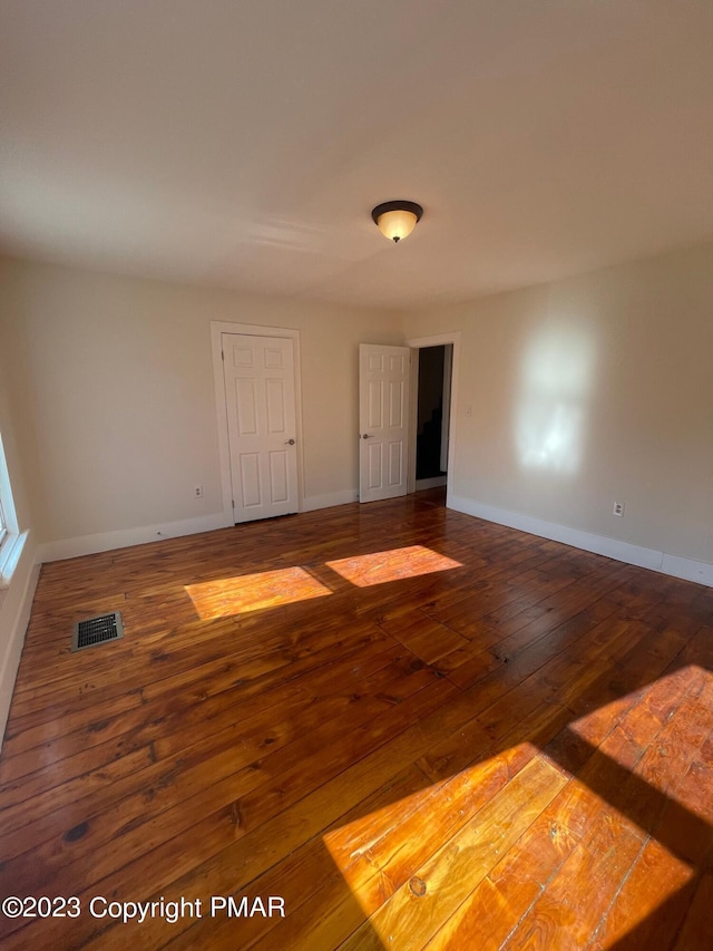 unfurnished room featuring hardwood / wood-style flooring, visible vents, and baseboards